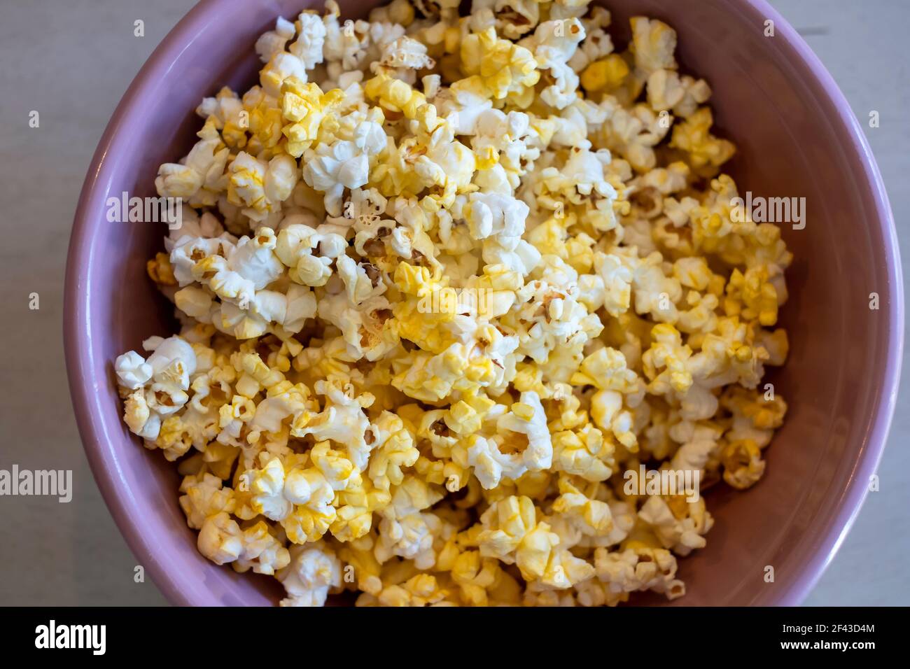 Popcorn, or popped corn, in a pink bowl on a table. Stock Photo