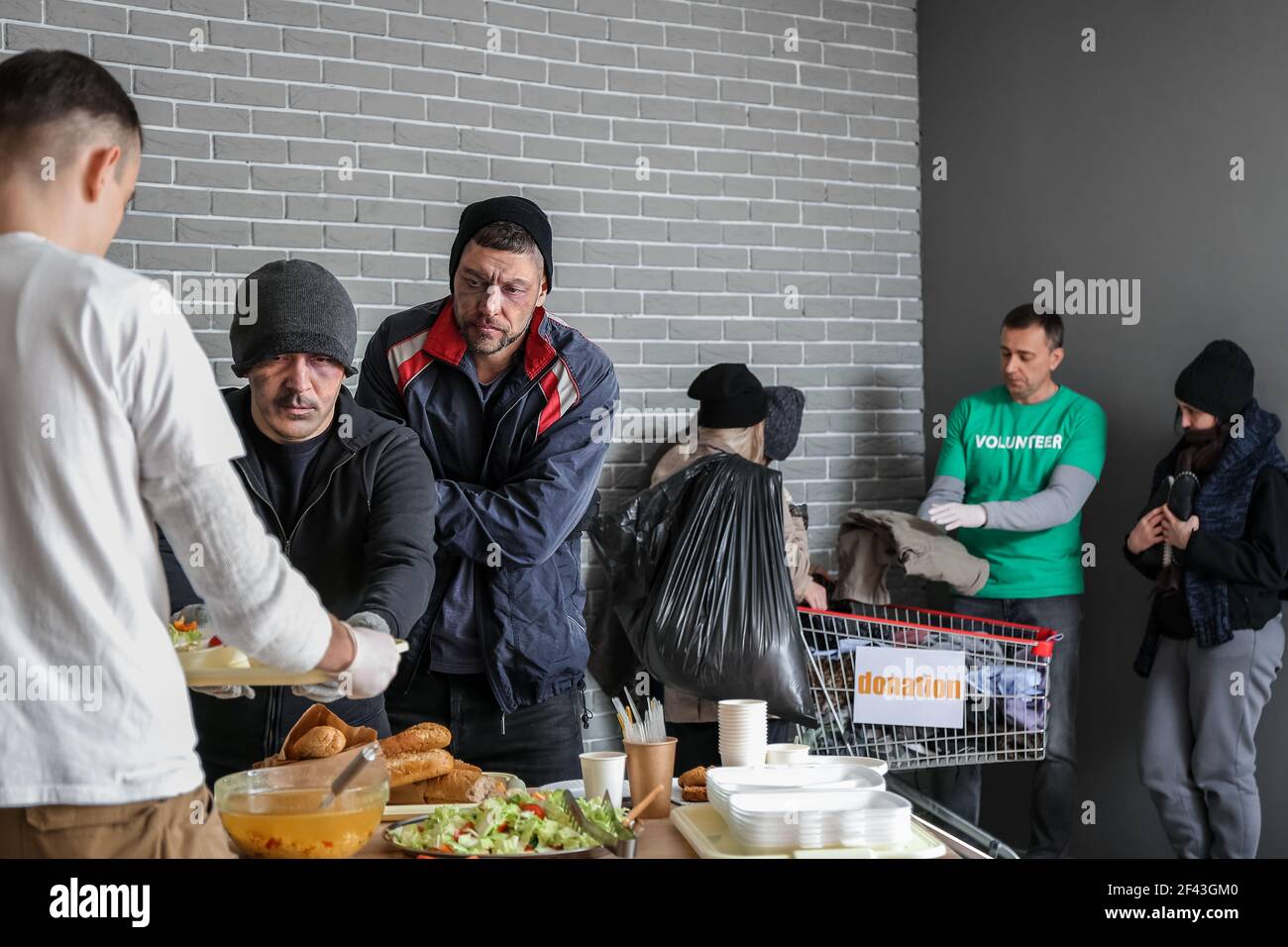 Volunteers giving food and clothes to homeless people in warming center