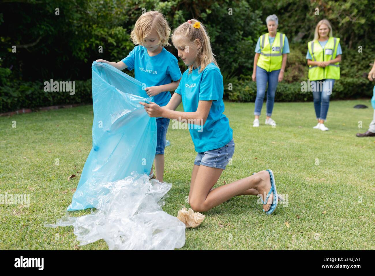 Caucasian boy and girl with volunteer group kneeling collecting plastic rubbish in field Stock Photo