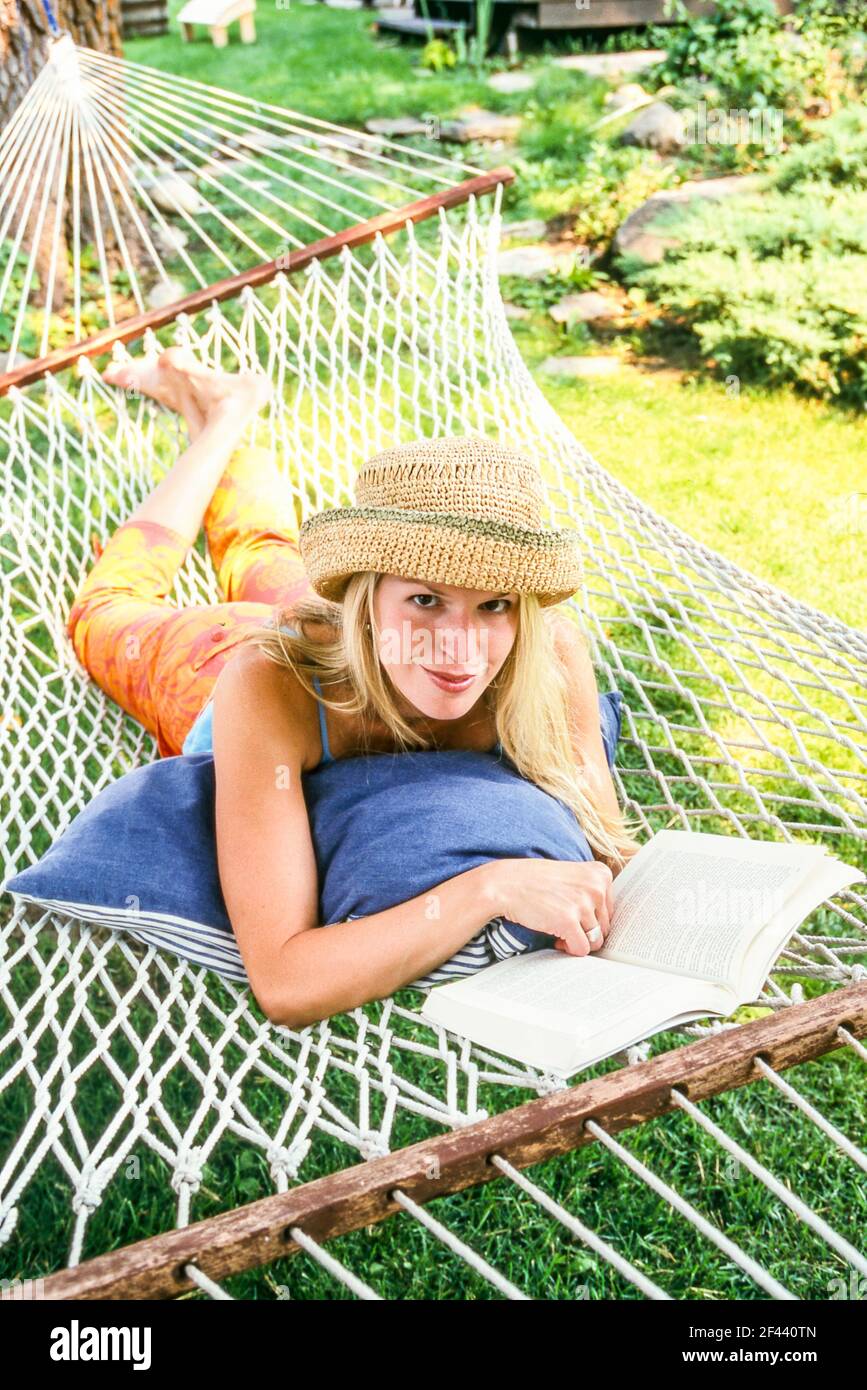 A woman reading a book while relaxing on a hammock outdoors. Stock Photo