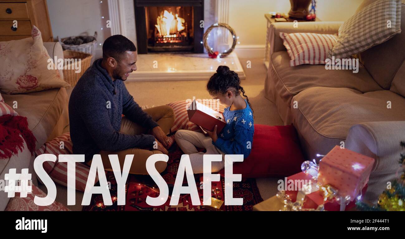 Stay safe text over father with daughter opening present at christmas Stock Photo