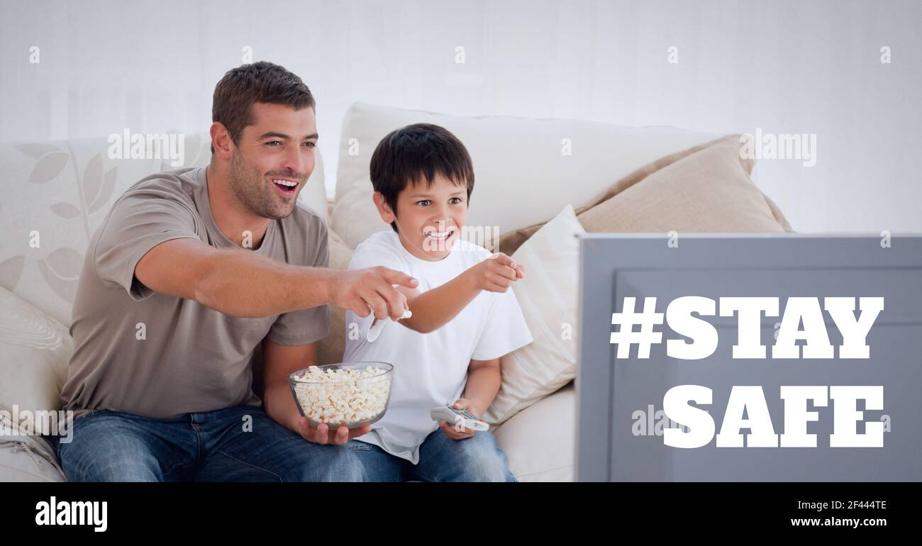 Stay safe text over father and son watching television and eating popcorn Stock Photo