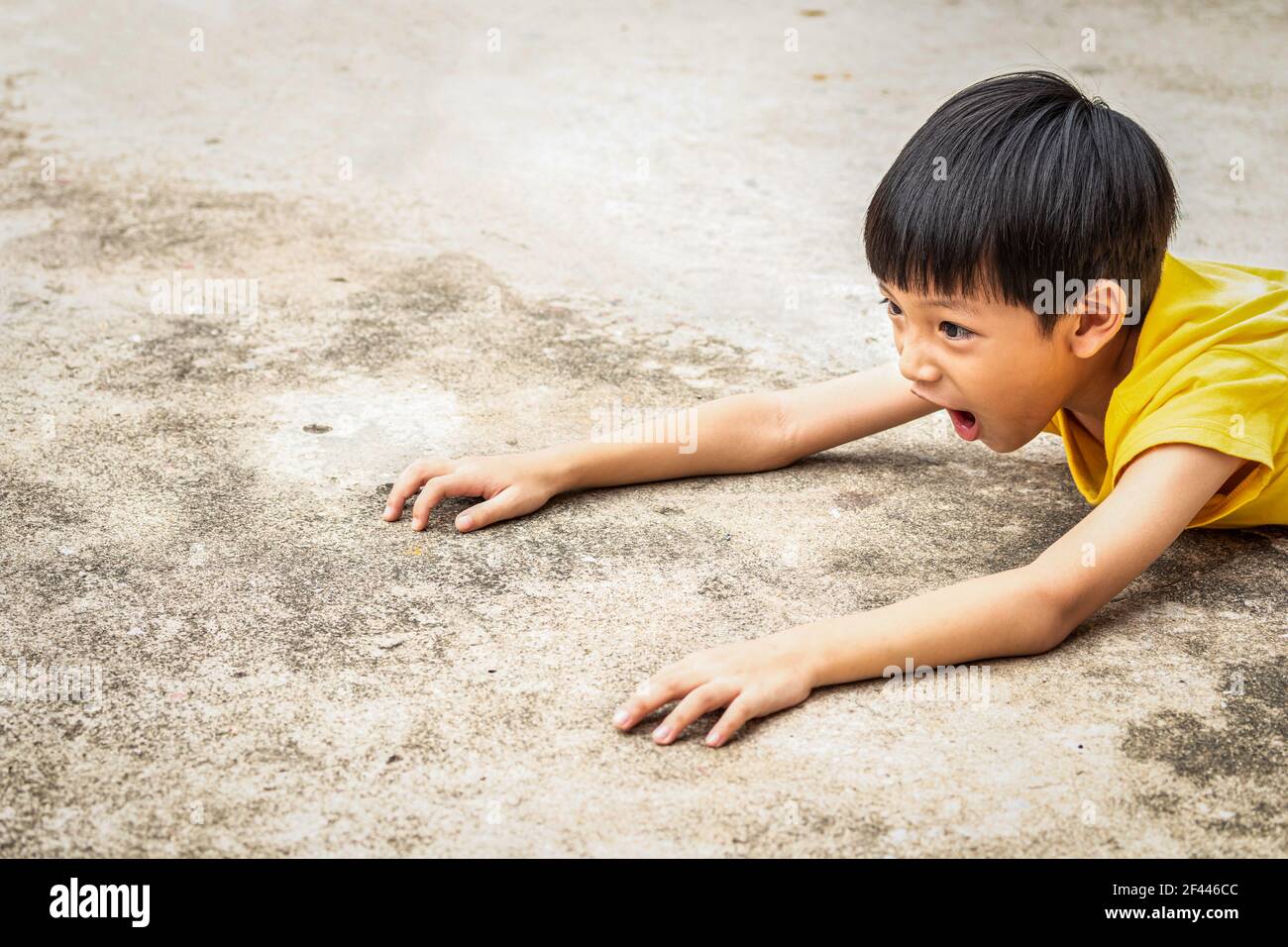 The boy falls to the cement floor. Making a very shocked face. The Asian child fell to the ground because he ran carelessly. The kid was stumbling on Stock Photo
