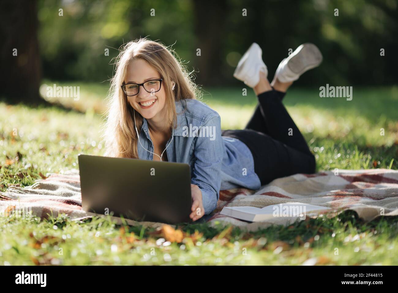 Woman lying at park and surfing internet on laptop Stock Photo