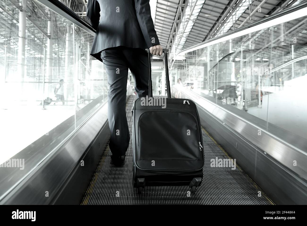 Businessman holding trolley bag going up on the escalator at the airport Stock Photo