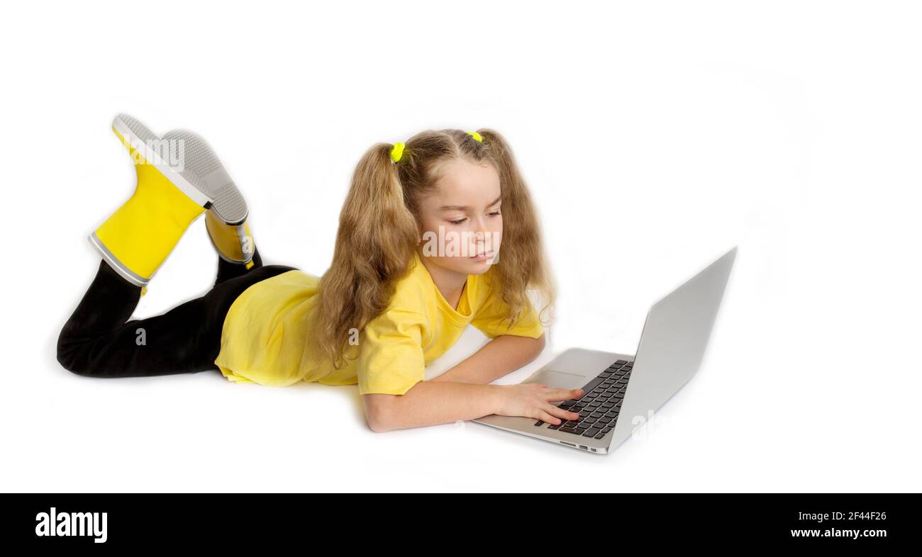 Concentrated cute girl child yellow t-shirt lying in front of computer, checking tasks in online classroom, e-learning distance learning concept. Stock Photo