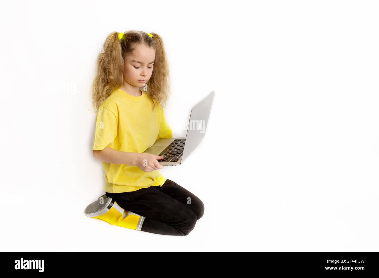Concentrated cute european girl child in yellow t-shirt sitting with laptop checking tasks in online class, e-learning distance learning concept. Stock Photo