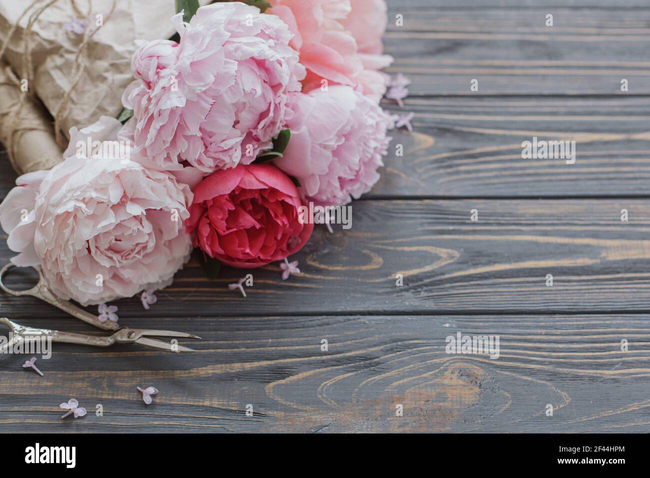 Beautiful stylish peony bouquet in paper, twine and scissors on rustic dark wooden background, copy space. Happy Mothers day greetings. Pink and white Stock Photo