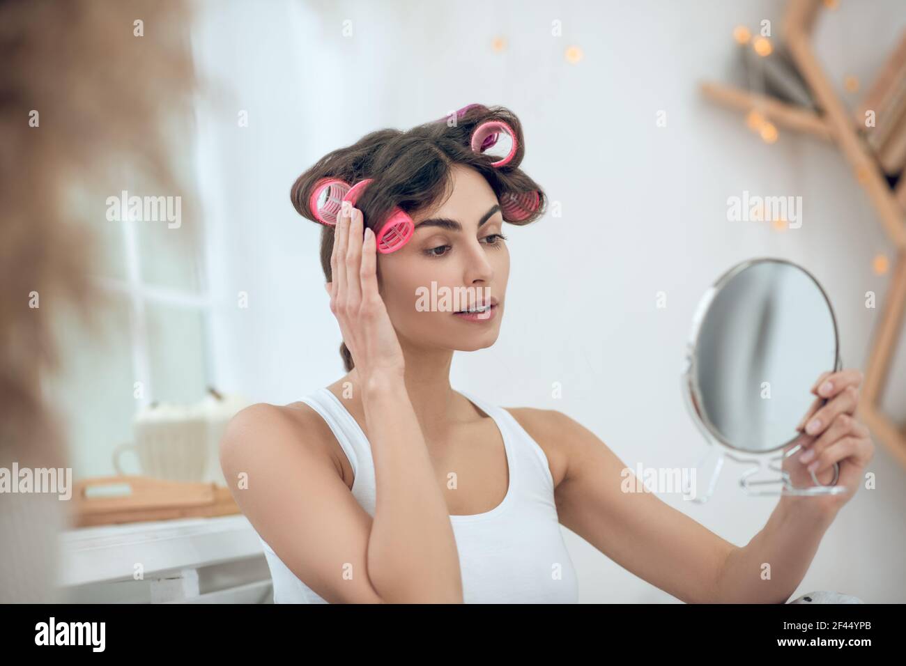 Nice-looking woman in curlers looking at herself in mirror Stock Photo