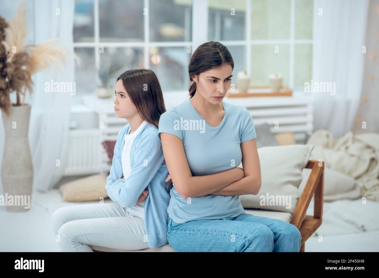 Mom and daughter sitting turned away from each other Stock Photo