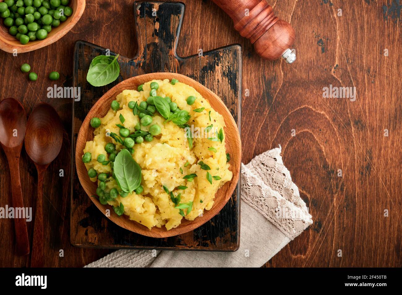 Mashed potato with butter, green peas, onions, basil on a rustic wooden background. Top view with close up. Stock Photo