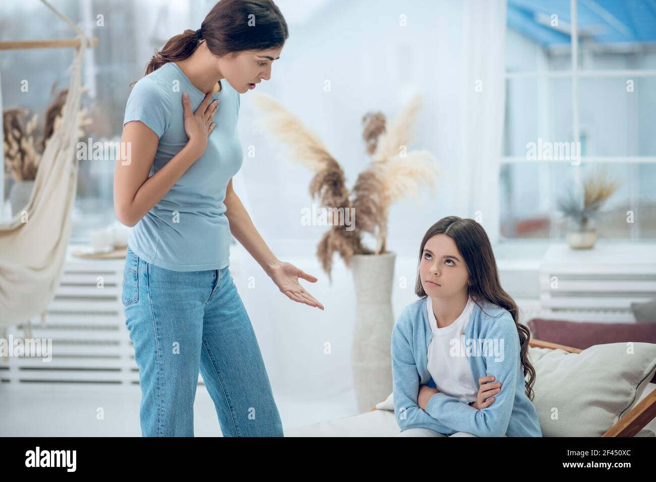 Standing talking mom and sitting naughty daughter Stock Photo