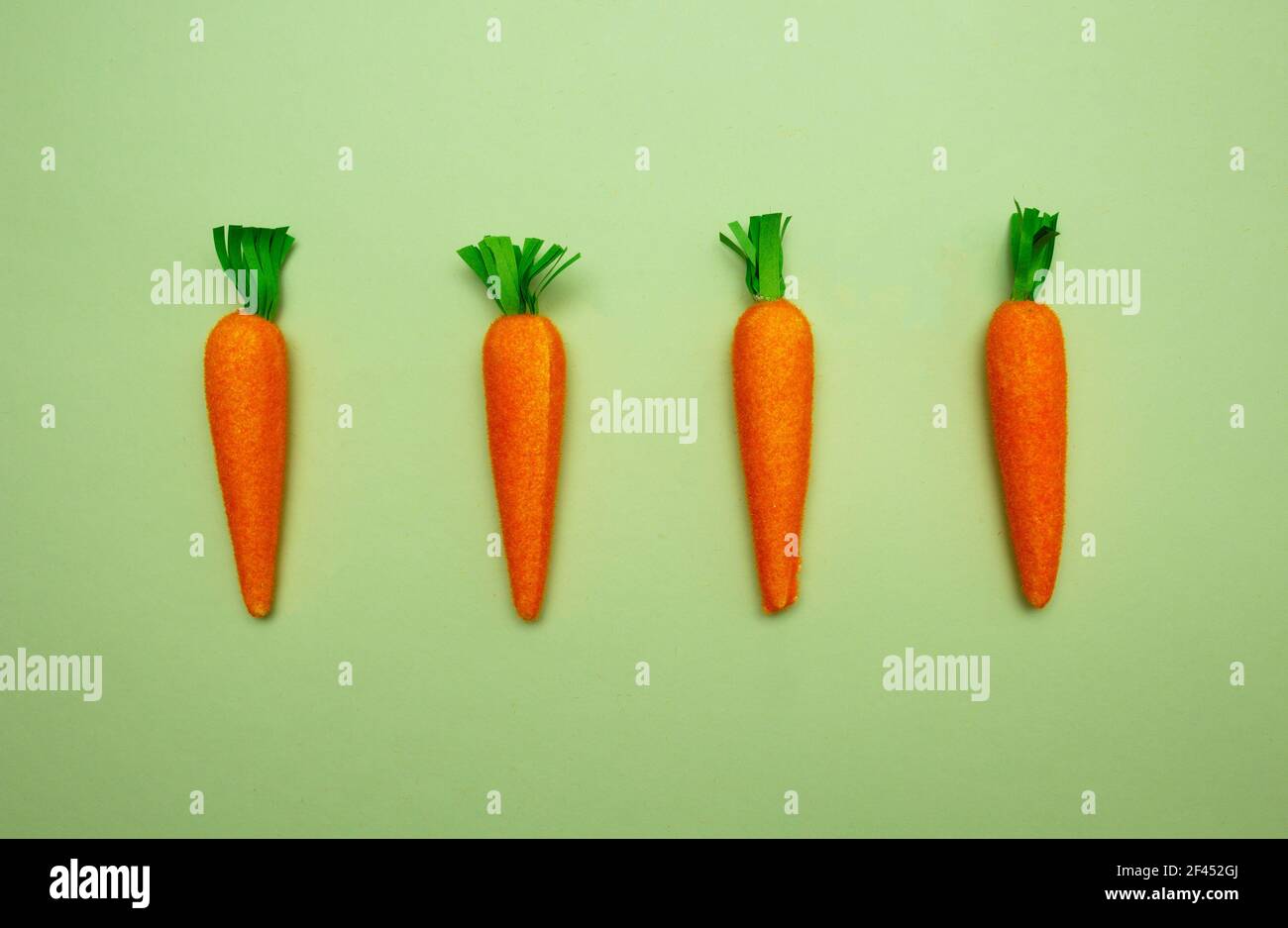 Four fake carrots on green background. Easter, spring holidays concept
