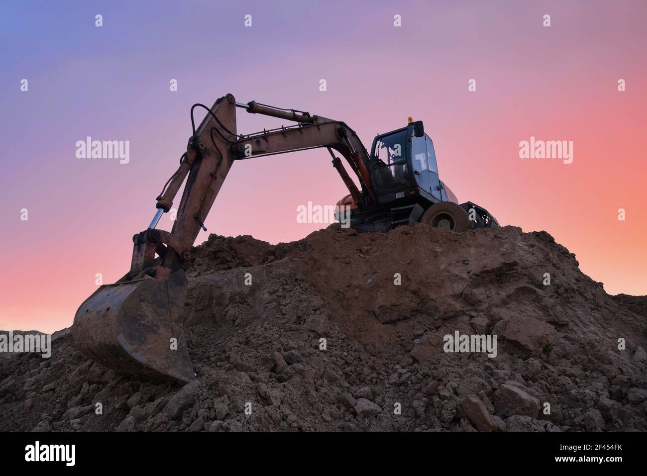 Excavator working on earthmoving at open pit mining on sunset