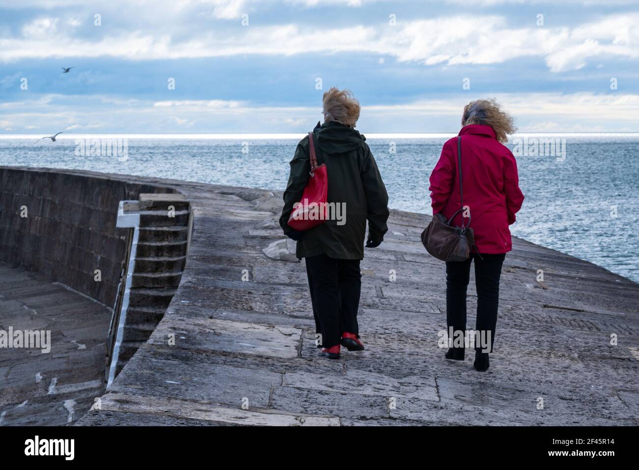 Lyme Regis, Dorset, UK. 19th March 2021. UK Weather: Sunshine and cloud along with a chilly breeze at the seaside resort of Lyme Regis. People take a brisk walk along the Cobb, but a  bracing sea breeze kept many people away. Credit: Celia McMahon/Alamy Live News. Stock Photo