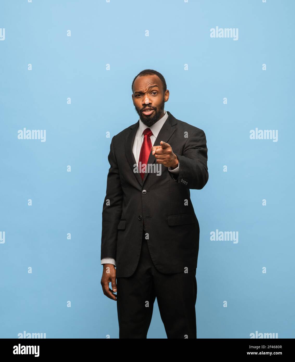 Portrait of young African-American man in black suit isolated on blue ...