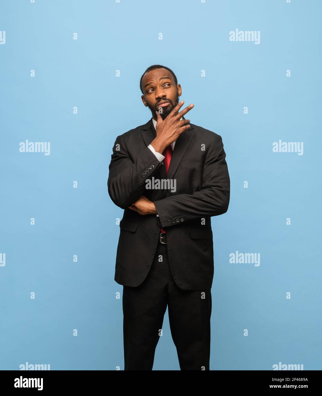 Portrait of young African-American man in black suit isolated on blue ...