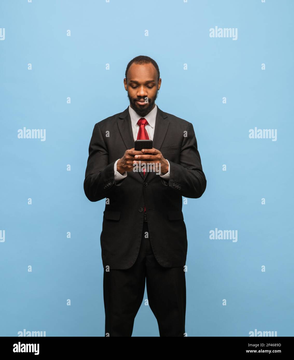 Serious young African-American man in black suit isolated on blue ...