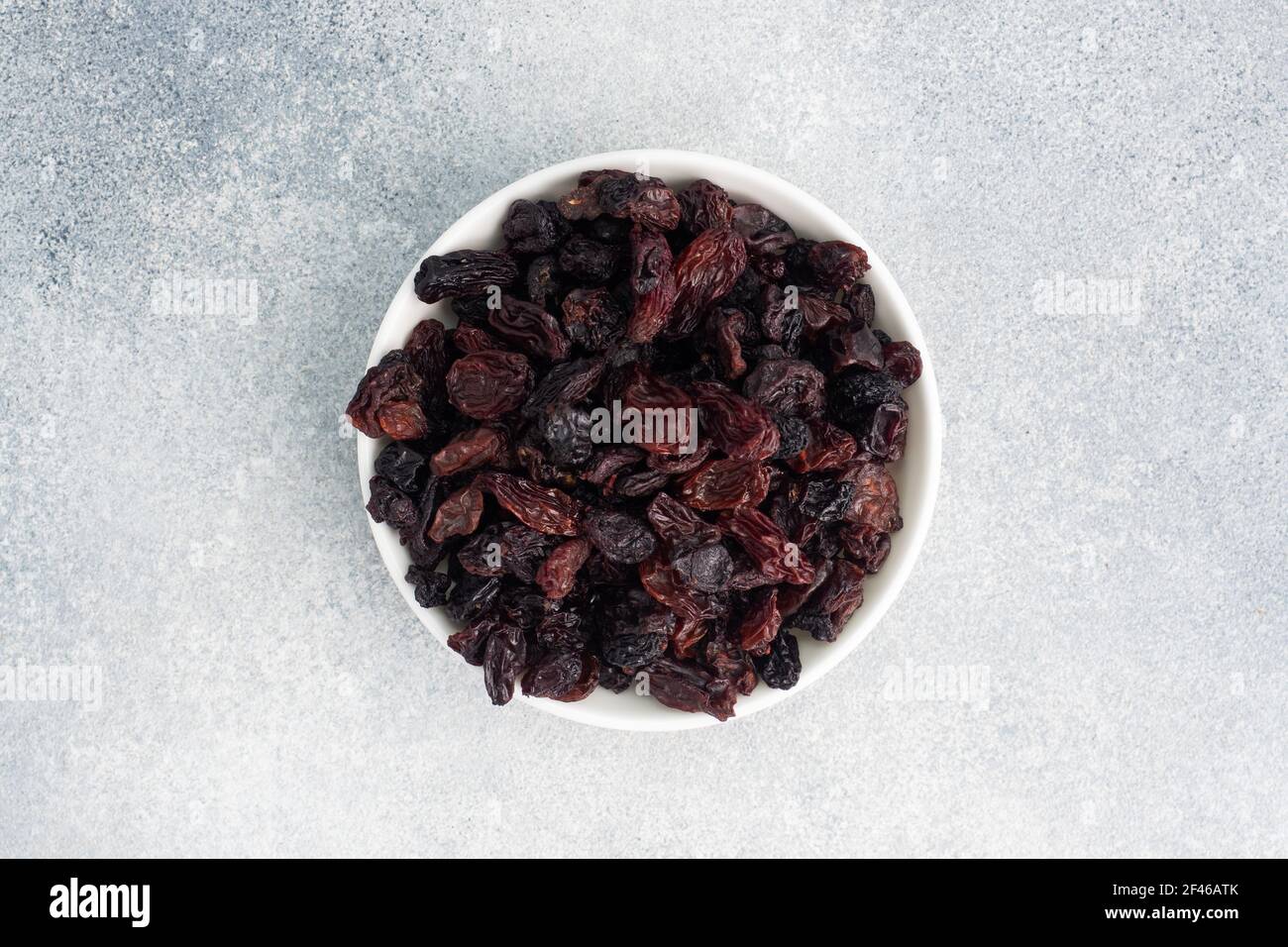 Dried raisins from dark grapes in a plate on a gray concrete background, copy space top view Stock Photo
