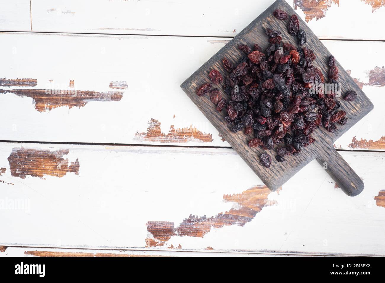 Dried raisins from dark grapes in a plate on a wooden chopping board Stock Photo