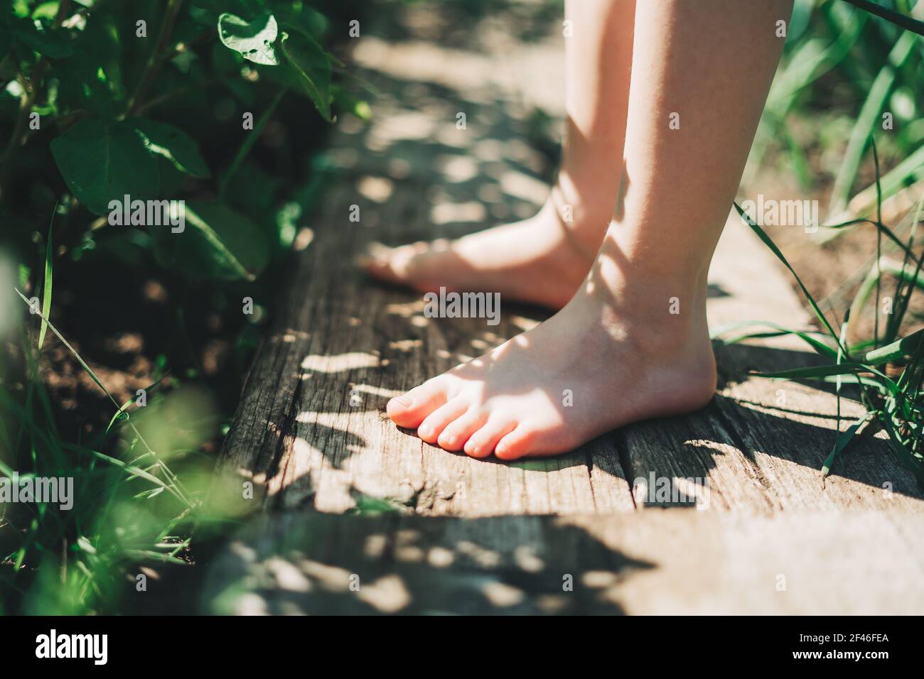 Kid walking barefoot on wood plank at a grass field Stock Photo