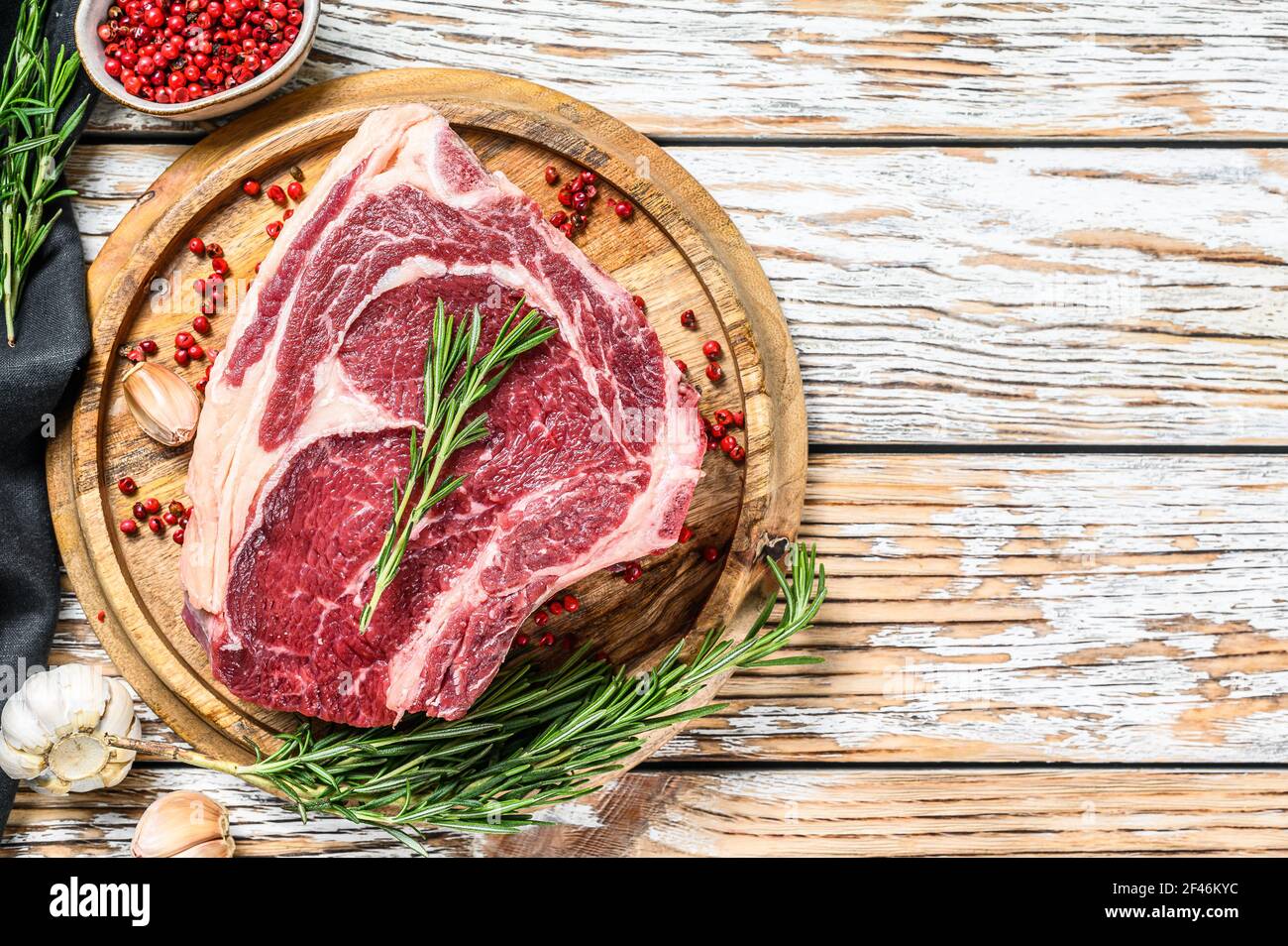 Raw cowboy steak or ribeye on the bone on a cutting board. Marble beef. White wooden background. Top view. Copy space Stock Photo