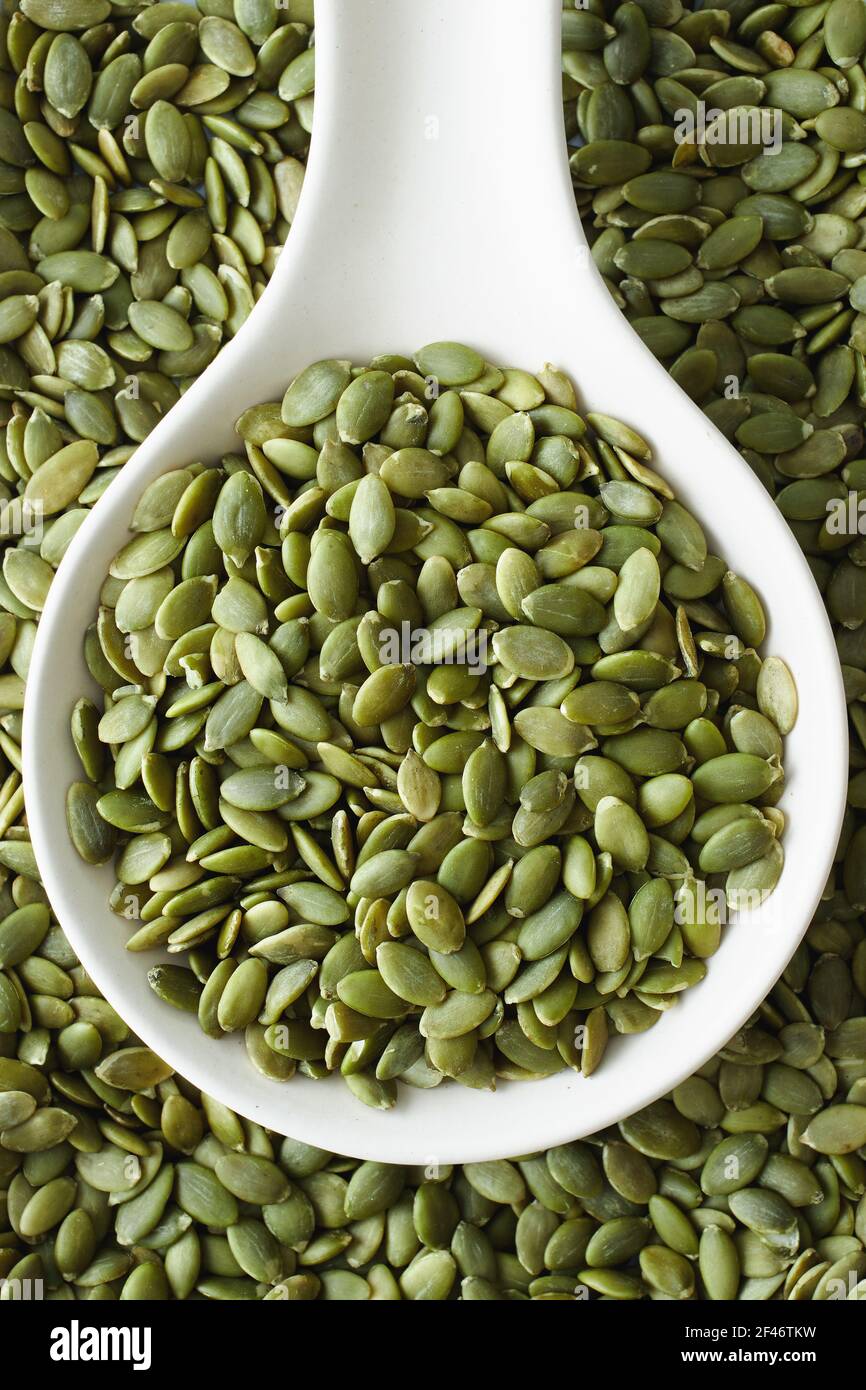 Pumpkin seeds on and beside white spoon Stock Photo