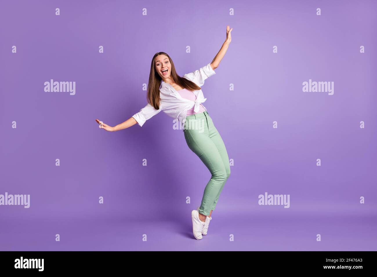 Photo of funky amazed girl stand tiptoes have fun wear sneakers pants white shirt isolated purple color background Stock Photo