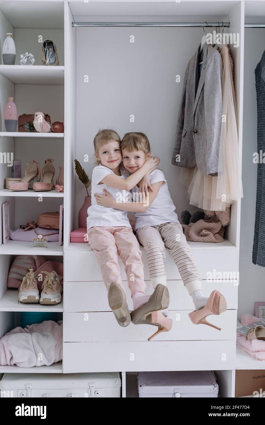 Family wardrobe. Happy twin sisters on shelve in closet with natural  organic clothes in cozy dressing room play joyfully Stock Photo - Alamy