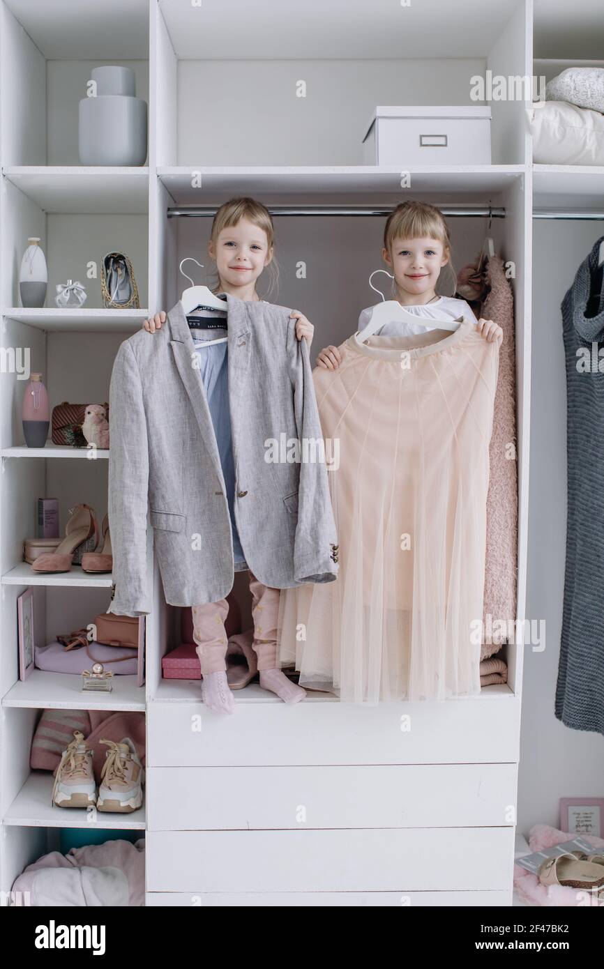Family wardrobe. Happy twin sisters on shelve in closet with natural  organic clothes in cozy dressing room play joyfully Stock Photo - Alamy