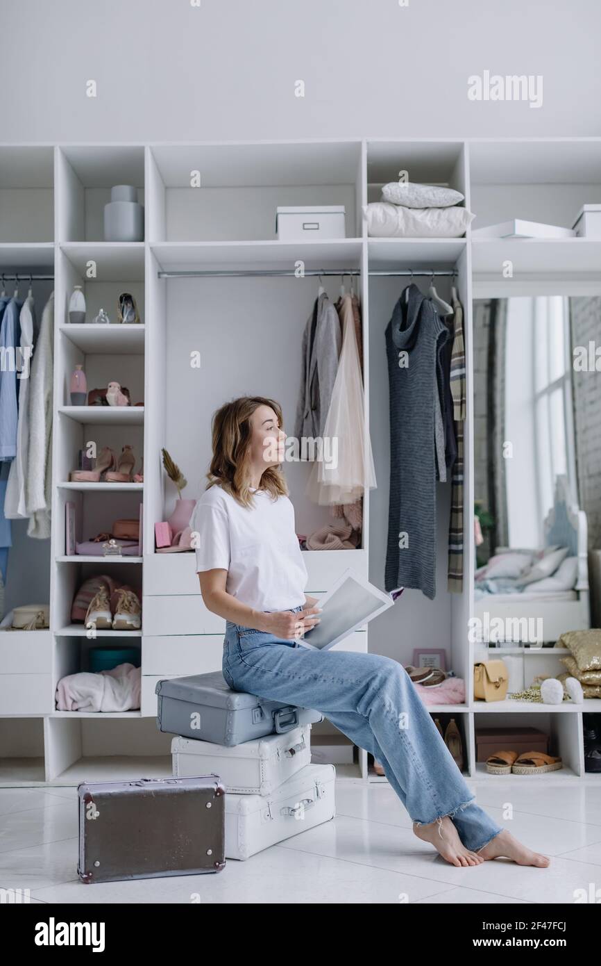 Stylish young female fashion designer dreaming sitting near wardrobe