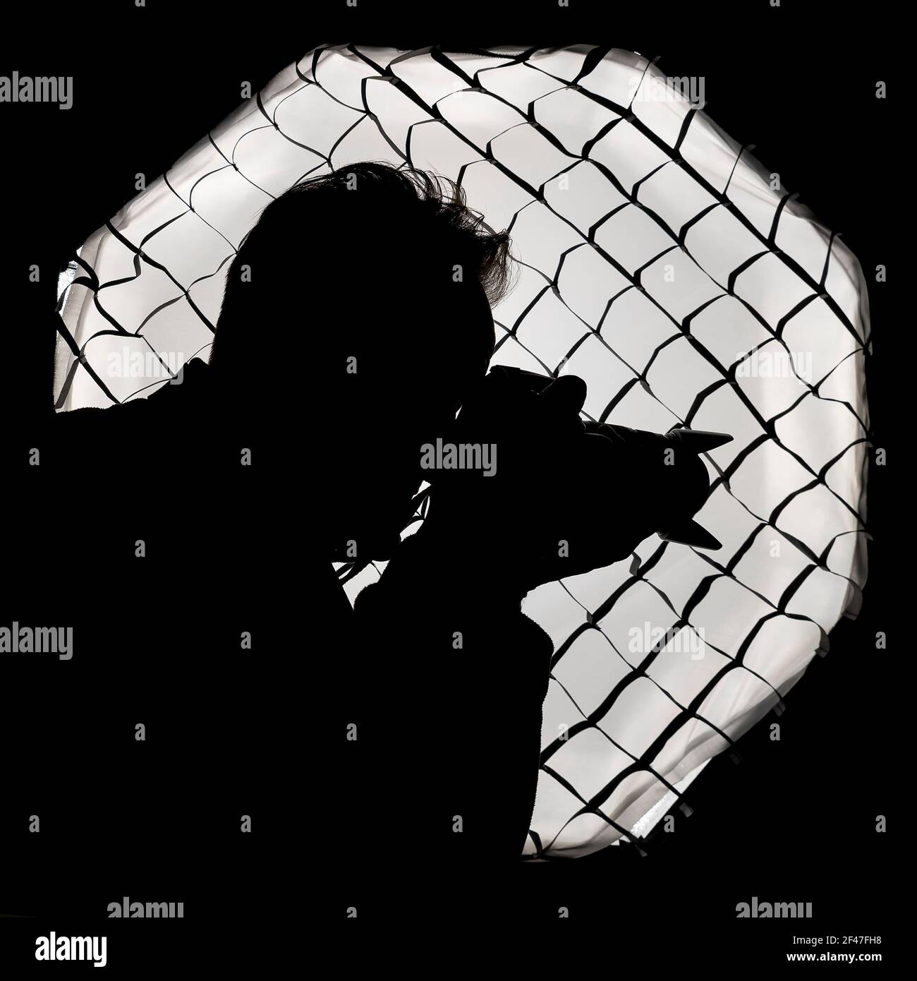 Silhouette of a photographer against a large light softbox with honeycomb grid, typical of a photo studio Stock Photo