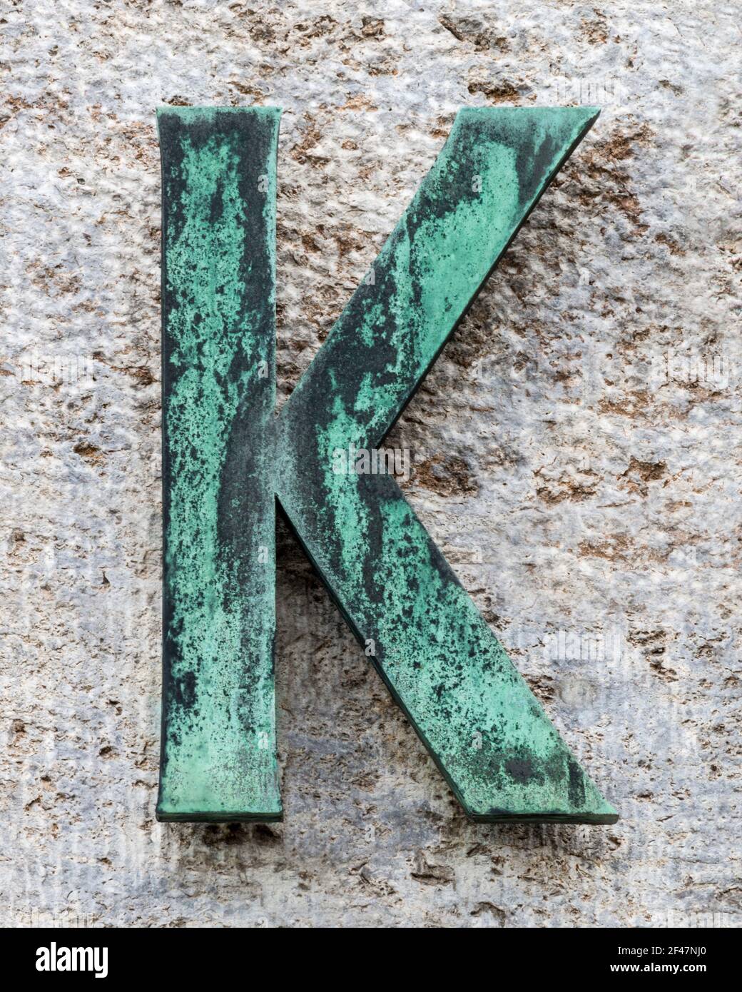 Metal letter K covered with verdigris on a natural stone wall Stock Photo