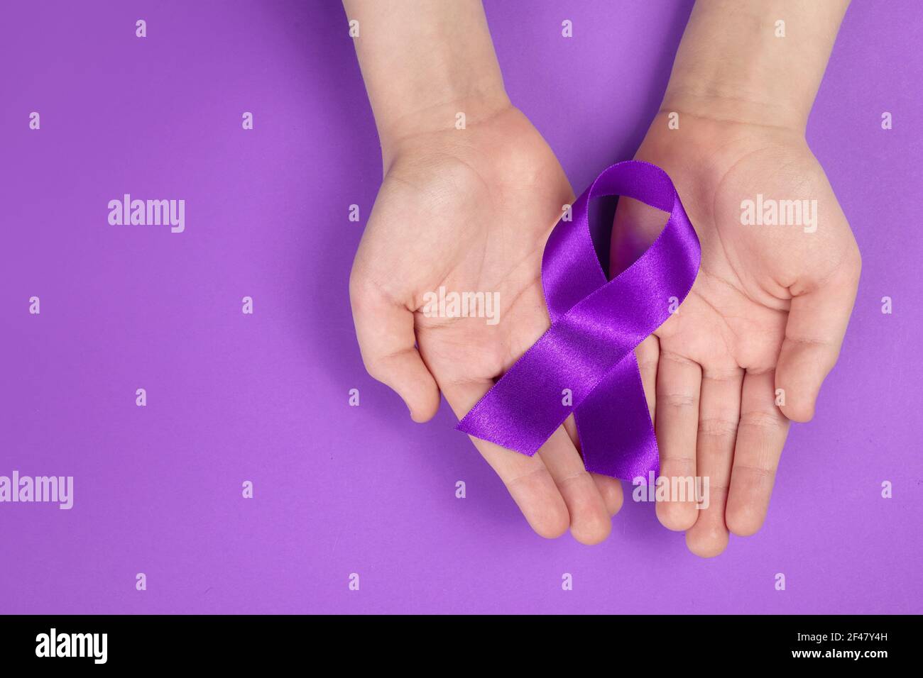 Purple day. World epilepsy day. Hands holding purple ribbon on purple background Stock Photo