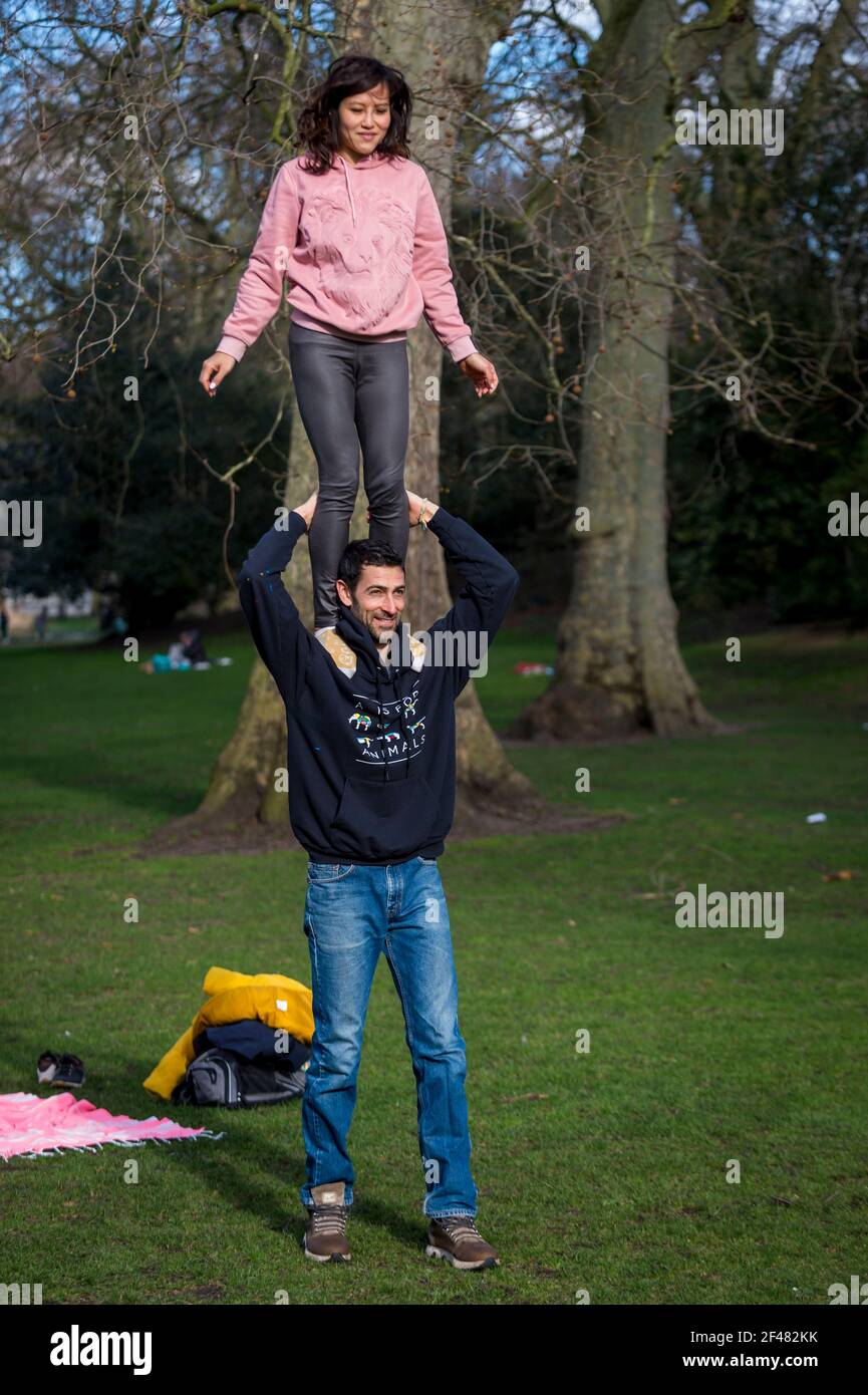 London, UK.  19 March 2021. UK Weather - Serena and Paul practice acro-yoga on a sunny spring day in St James’s Park.   The UK government is due to relax coronavirus lockdown restrictions allowing group indoor exercise, but for now the couple continue to exercise outdoors.   Credit: Stephen Chung / Alamy Live News Stock Photo