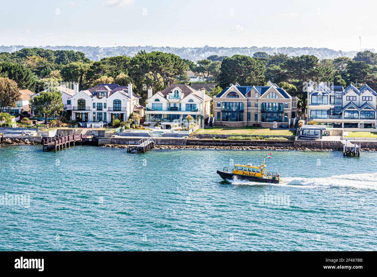 The harbourmaster's pilot boat passing luxury houses on the Sandbanks Peninsula in Poole Harbour, Dorset UK Stock Photo