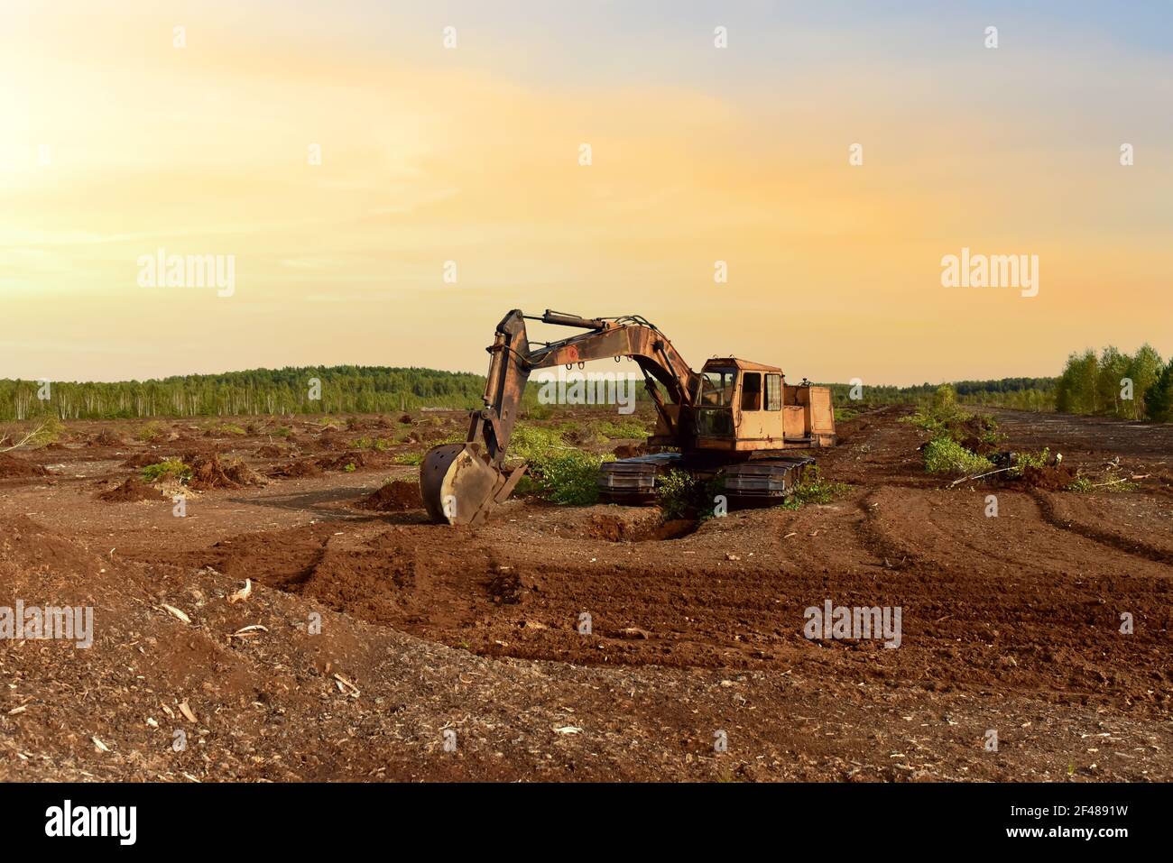 Excavator digging drainage ditch in peat extraction site. Drainage of peat bogs and destruction