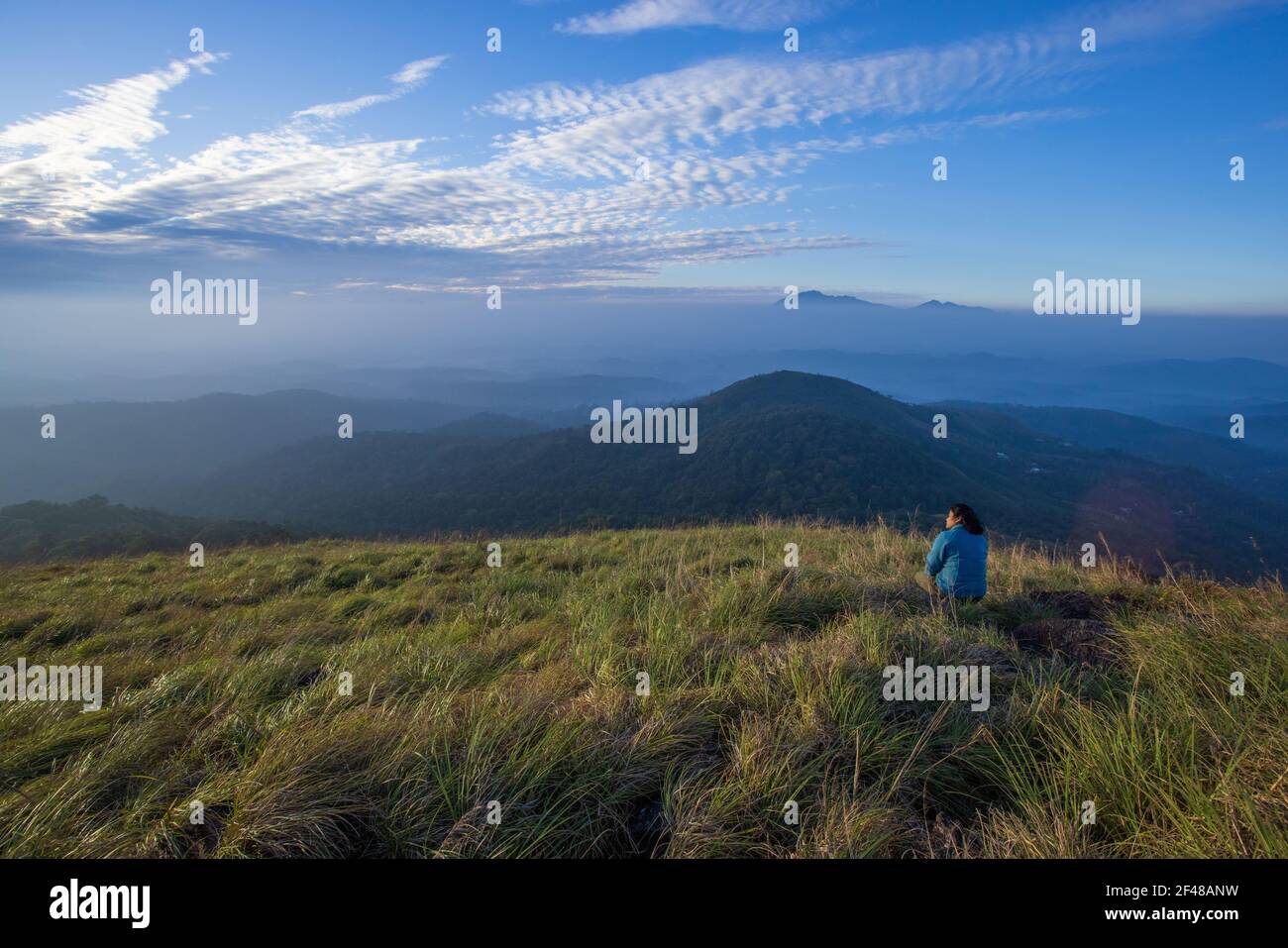 A lady enjoying the magnificent view from a hilltop in Wayanad during early morning (image taken in Wayanad, Kerala) Stock Photo