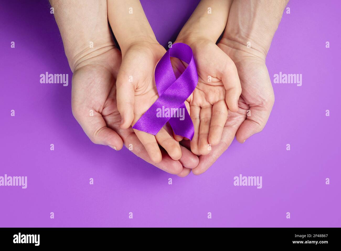 Purple day. World epilepsy day. Hands holding purple ribbon on purple background Stock Photo