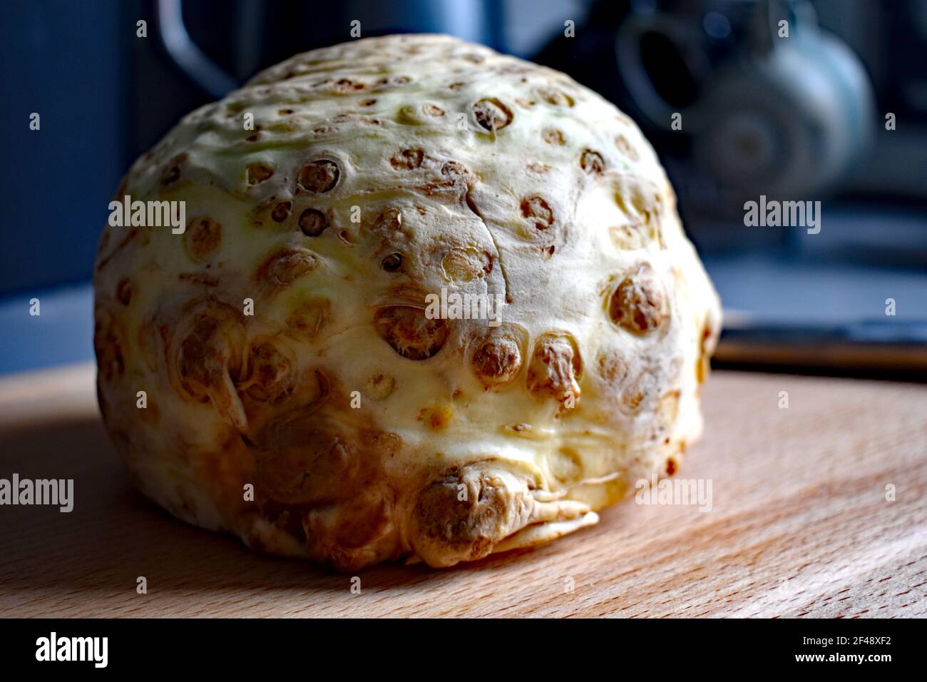 Celeriac, worlds ugliest vegetable, on a wooden chopping board, ceramic cups in the background. Stock Photo