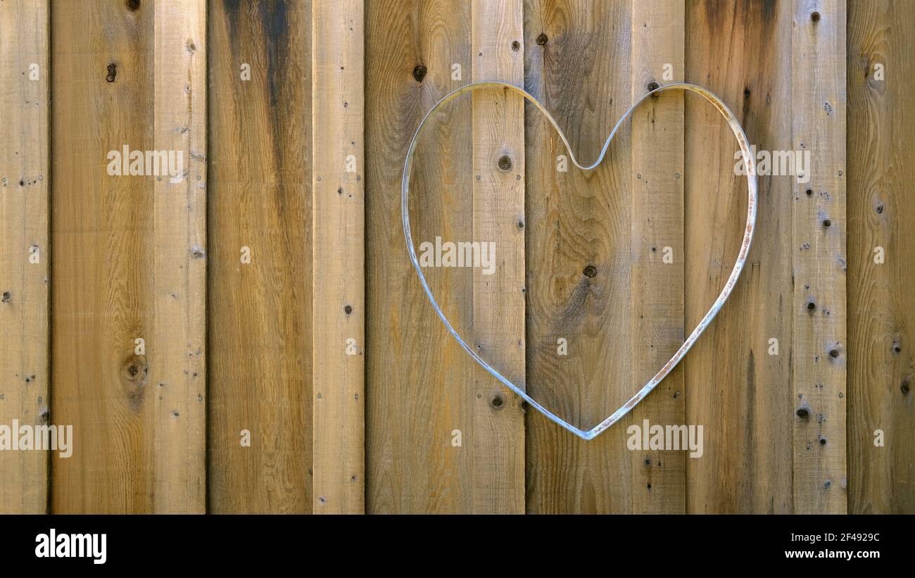 Metal shaped heart on a wood fence; hollow heart mold for decorating with flowers or lights; wedding or garden decoration and design. Stock Photo