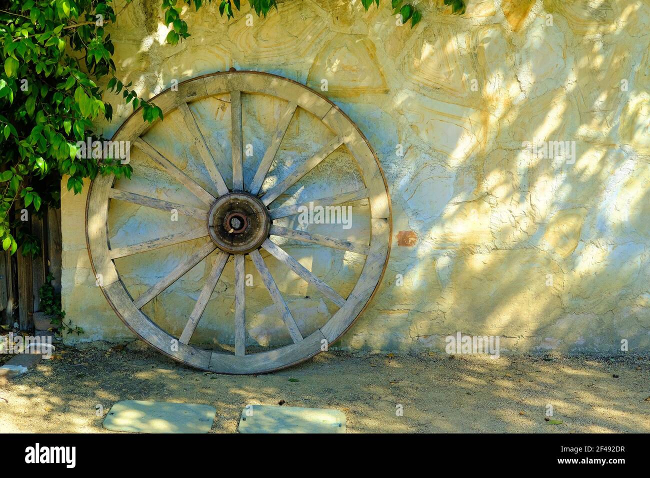 Wagon wheel leaning on a rustic wall; western, cowboy country decor and style. Stock Photo