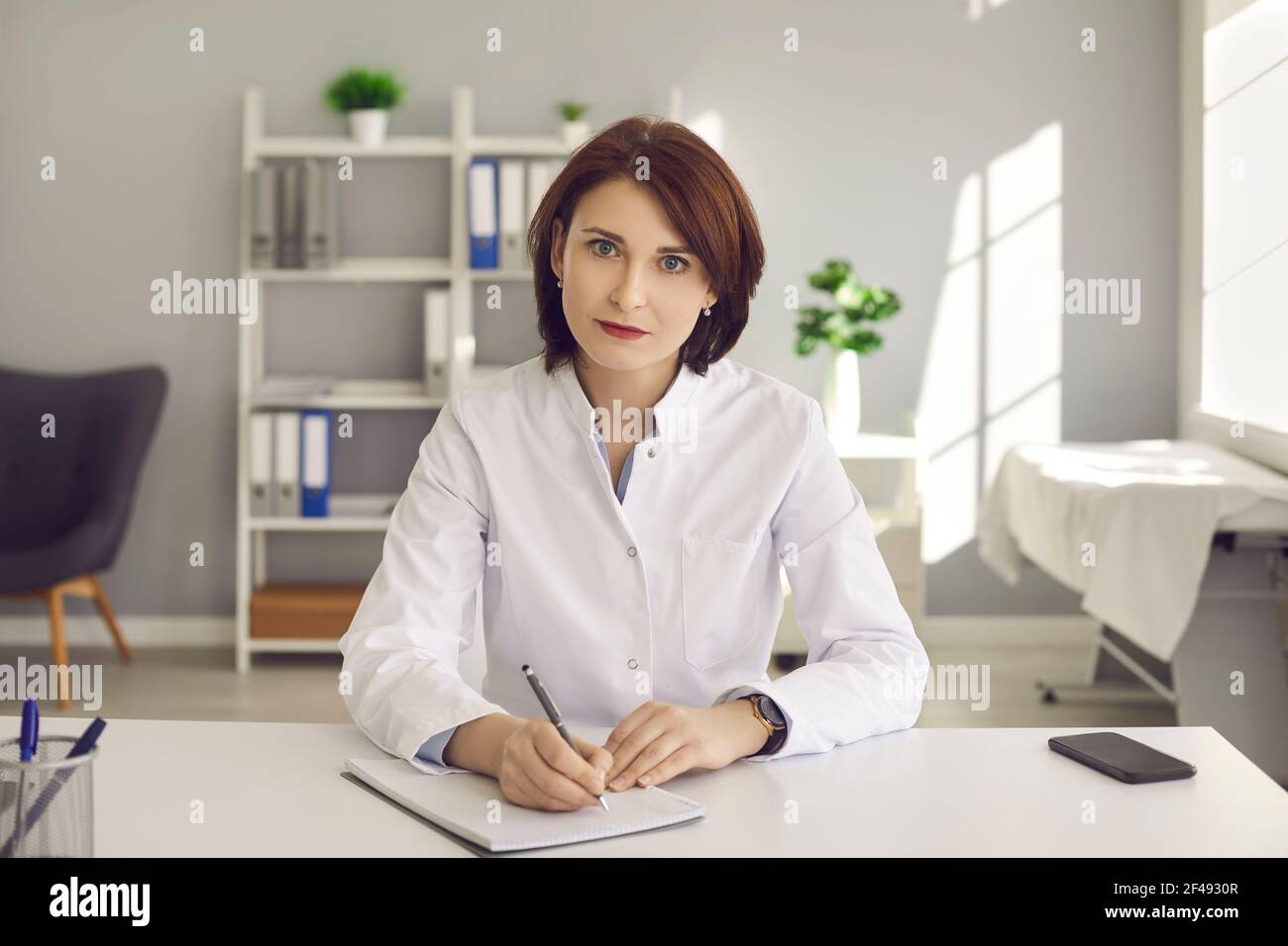 Female doctor writes notes during a video conference or listening to medical online training. Stock Photo