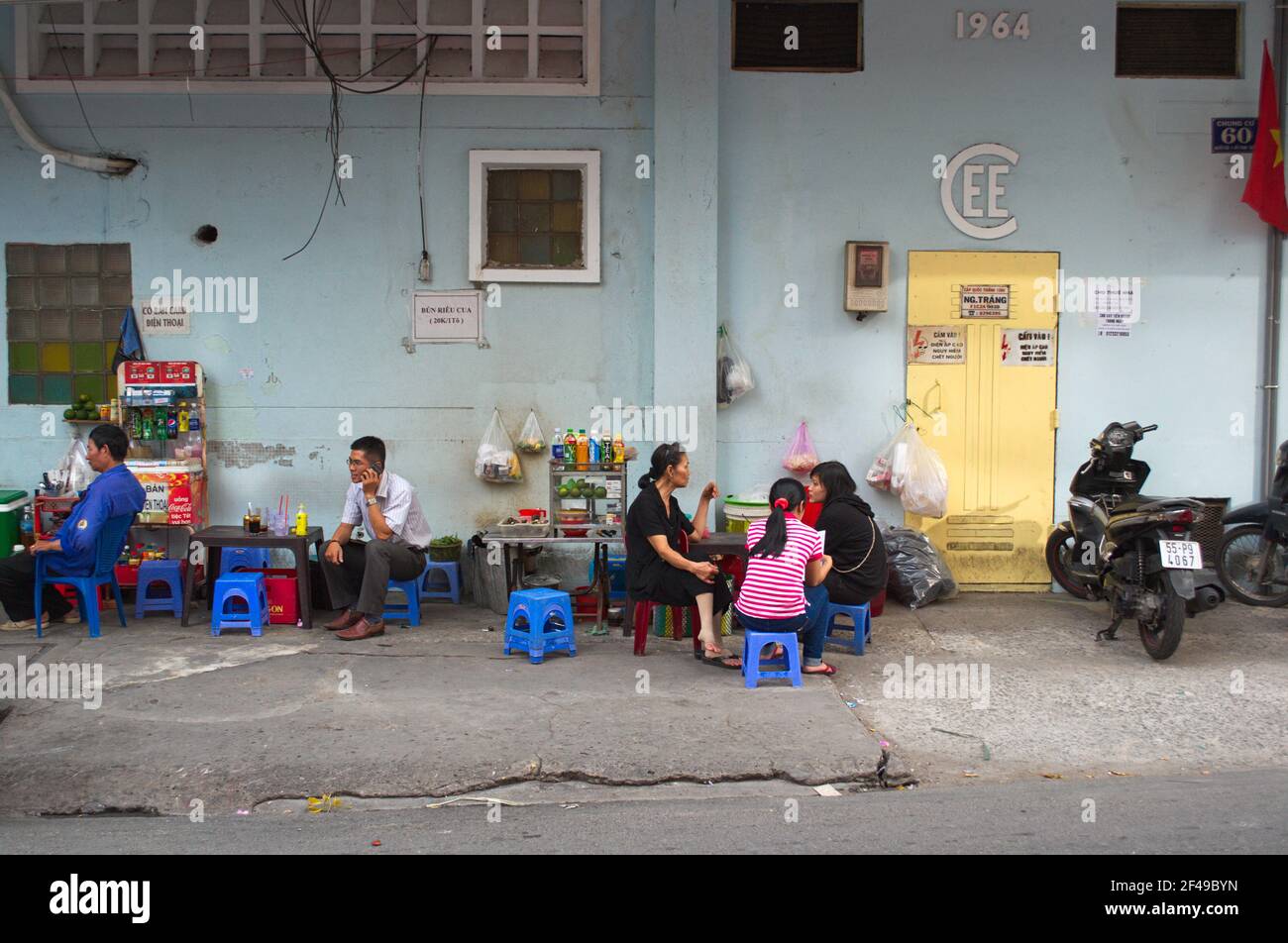 July, 2015 - Ho Chi Minh, Vietnam: People sitting on small chairs outside in street cafe along the road. Stock Photo
