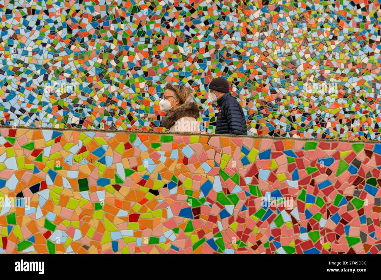 Dusseldorf, NRW, Germany. 19th Mar, 2021. Two people in FFP2/KN95 face masks walk past the 'Rivertime' mosaic wall by Hermann-Josef Kuhna on the banks of the river Rhine in Dusseldorf, capital of NRW. Lockdown measures are likely to once again increase in Germany as the 7-day incidence rate creeps up towards the crucial cut-off point of 100/100k inhabitants. Whilst Dusseldorf fares relatively well at 63 today, Germany overall saw numbers rise to 95.6 Credit: Imageplotter/Alamy Live News Stock Photo