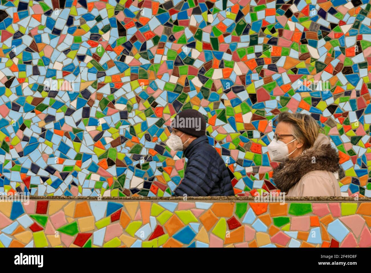 Dusseldorf, NRW, Germany, 19th Mar 2021. Two people in FFP2/KN95 face masks walk past the 'Rivertime' mosaic wall by Hermann-Josef Kuhna on the banks of the river Rhine in Dusseldorf, capital of NRW. Lockdown measures are likely to once again increase in Germany as the 7-day incidence rate creeps up towards the crucial cut-off point of 100/100k inhabitants. Whilst Dusseldorf fares relatively well at 63 today, Germany overall saw numbers rise to 95.6 Stock Photo