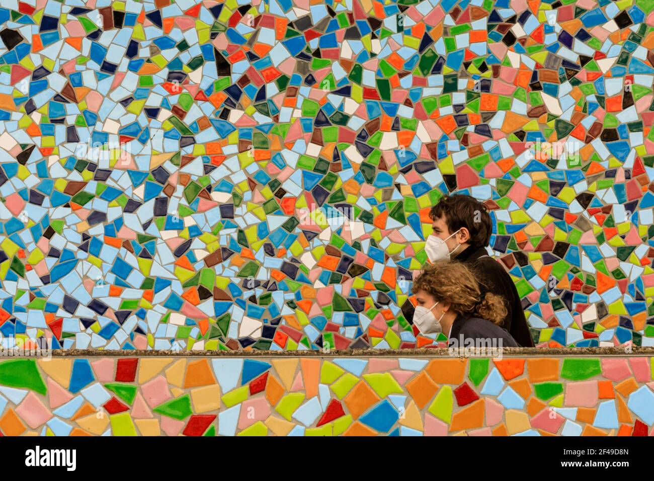 Dusseldorf, NRW, Germany, 19th Mar 2021. Two people in FFP2/KN95 face masks walk past the 'Rivertime' mosaic wall by Hermann-Josef Kuhna on the banks of the river Rhine in Dusseldorf, capital of NRW. Lockdown measures are likely to once again increase in Germany as the 7-day incidence rate creeps up towards the crucial cut-off point of 100/100k inhabitants. Whilst Dusseldorf fares relatively well at 63 today, Germany overall saw numbers rise to 95.6 Stock Photo