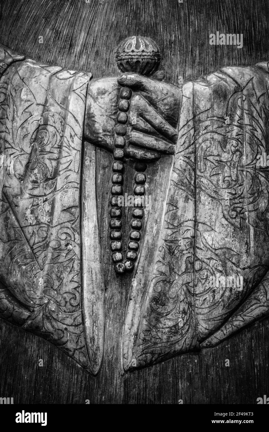 Spiritual arat a carving of hands holding prayer beads, arms covered by textured sleeves Stock Photo
