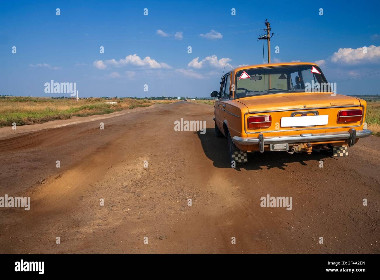 Old Soviet car of the USSR of orange color, on a bad rural road among ...