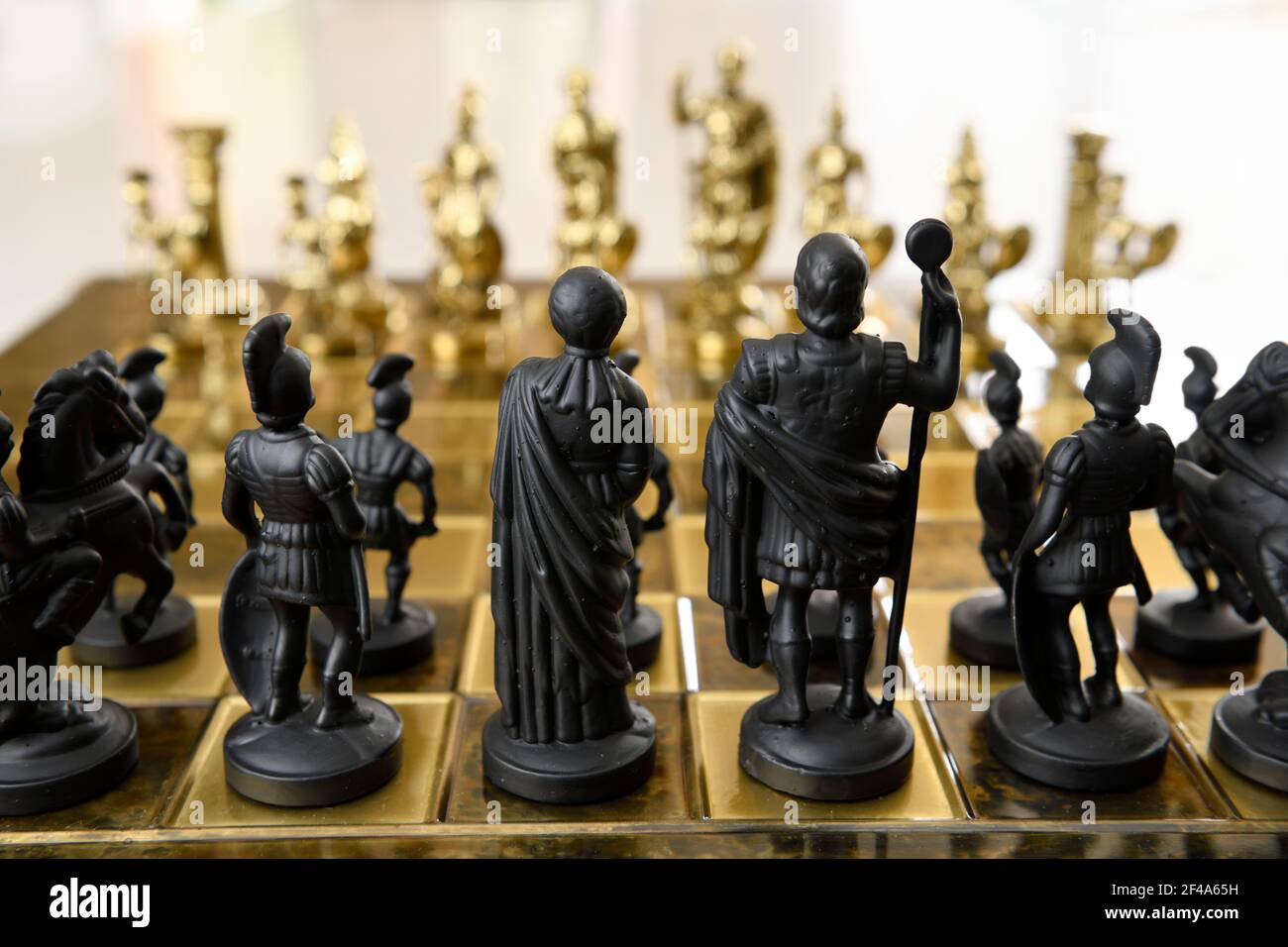 Back of black queen king centurion and knight chess piece figurines on chessboard facing gold opposing army Stock Photo